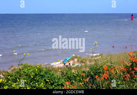 La plage de couleur vive umbrellla offre de l'ombre lors d'une journée chaude en juillet à South Haven, Michigan. Les amateurs de plage apprécient la vue lointaine de South Haven Banque D'Images