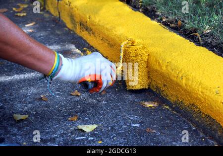 L'employé repeint le côté curbside jaune. Il utilise un rouleau à peinture et porte des gants. Banque D'Images