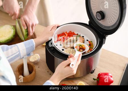 Femme cuisant du poisson savoureux dans une cuisinière multiple, gros plan Banque D'Images