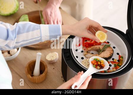 Femme pressant le citron sur le poisson dans une cuisinière multiple Banque D'Images