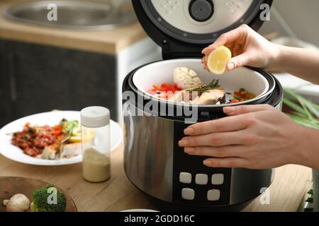 Femme pressant le citron sur le poisson dans une cuisinière multiple Banque D'Images