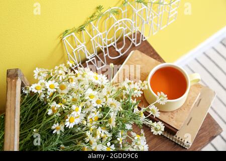 Boîte avec des chamomiles, des livres et une tasse de thé sur la table près du mur de couleur Banque D'Images