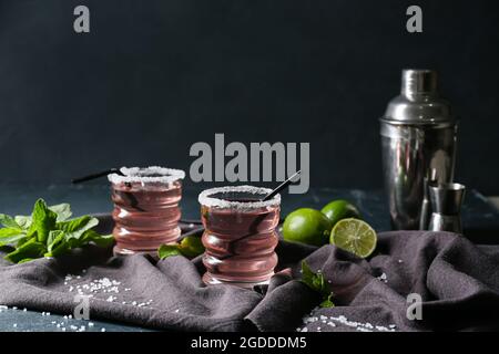 Composition avec verres de délicieux cocktail cosmopolite, shaker, limes et menthe sur fond sombre Banque D'Images