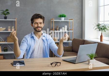 Jeune homme assis à son bureau de travail et méditant pour se calmer et réduire le stress Banque D'Images