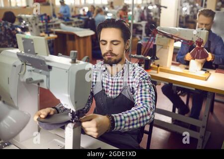 Ouvrier d'usine travaillant assis à table avec machine à coudre industrielle dans la salle d'atelier. Banque D'Images