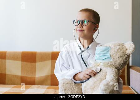 Mignon petit garçon caucasien jouant un jeu drôle comme le docteur tenant stéthoscope à l'écoute de jouet preschooler prétendant être une infirmière doux traiter patient à la maison. Dans une robe de chambre et un masque médical. Banque D'Images