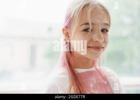 Portrait d'une petite fille blonde de l'adolescence portant un tablier dans la cuisine Banque D'Images