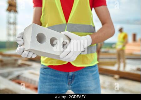 Bricklayer en gants de coton et gilet de protection debout à l'extérieur Banque D'Images
