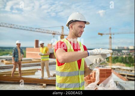 Couche de briquetage sérieuse dans un casque de chantier qui teste la qualité du matériau de construction Banque D'Images