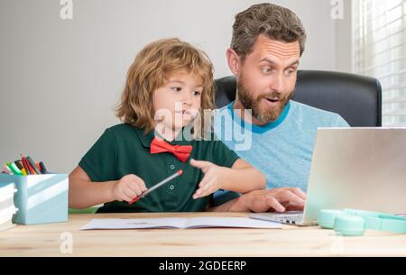 le père et l'enfant fils étonnés à l'école travaillant en ligne sur ordinateur portable, étonnement Banque D'Images