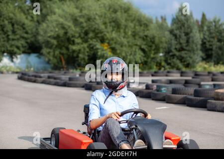 Une fille ou une femme dans un casque de sécurité se déplace un kart sur une piste spéciale clôturée avec des roues en caoutchouc. Activités sportives et de loisirs dans les transports. Préparation a Banque D'Images