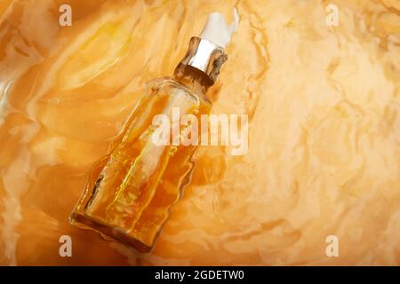 Flacon en verre avec du sérum de vitamine C orange flottant dans l'eau en mouvement Banque D'Images