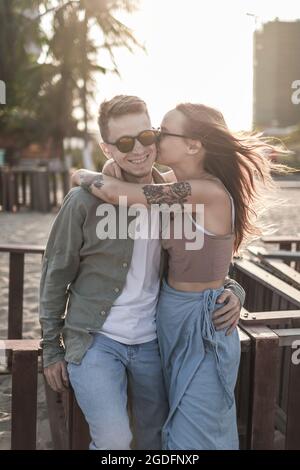 Charmant couple élégant souriant et embrassant sur la plage. De belles lumières solaires. Portrait. Millénaire. Porter des vêtements décontractés et des lunettes de soleil. Haute qualité Banque D'Images