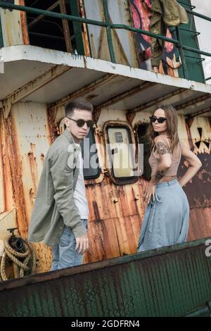 Jeune couple charmant sur le vieux navire debout. Porter des vêtements décontractés et des lunettes de soleil. Tatouages. Photo de haute qualité Banque D'Images