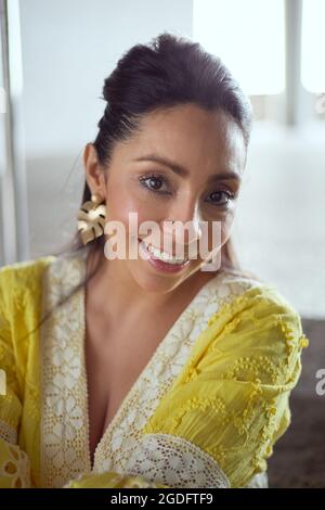 Portrait d'une jeune femme latine dans une robe jaune en regardant l'appareil photo avec un grand sourire Banque D'Images