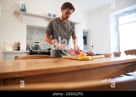 Young man slicing fresh watermelon à table de cuisine Banque D'Images