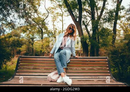 Femme élégante avec de longs cheveux blonds assis sur le banc de parc, portrait Banque D'Images