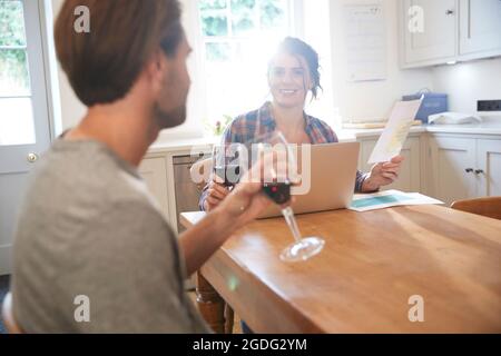 Table de cuisine à couple drinking red wine alors que doing paperwork Banque D'Images