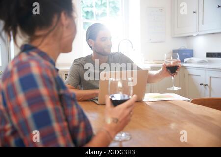 Table de cuisine à couple drinking red wine while using laptop Banque D'Images