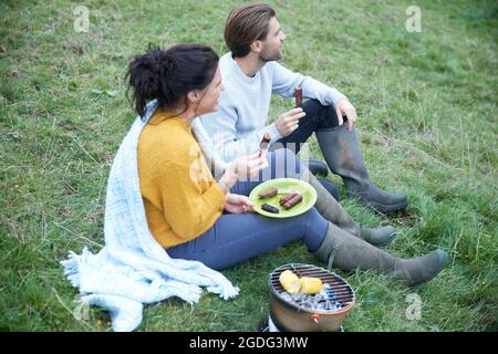 Couple sitting in rural field having barbecue Banque D'Images