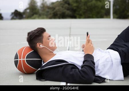 Joueur de basket-ball chez les hommes se trouvant sur un terrain de basket-ball looking at smartphone Banque D'Images