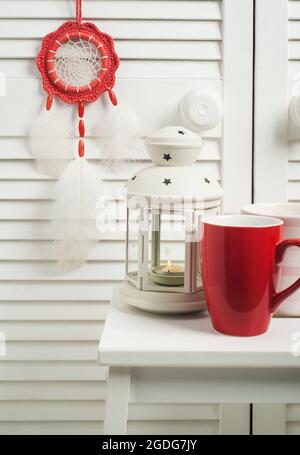 Rouge Dream Catcher avec plumes blanches à l'intérieur avec mug rouge et bougie allumée Banque D'Images