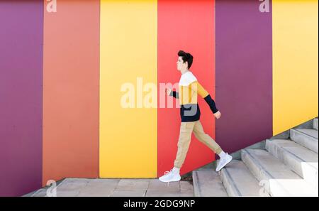 Adolescent descendant des escaliers à l'extérieur contre un mur coloré Banque D'Images