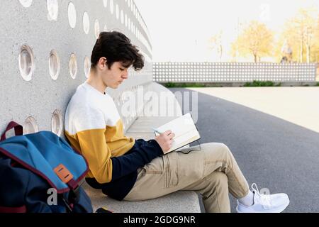 Un jeune homme écrit des notes dans un carnet assis sur un banc Banque D'Images