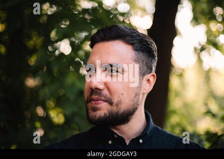 Portrait en gros plan de l'homme heureux confiant debout contre les arbres en été Banque D'Images