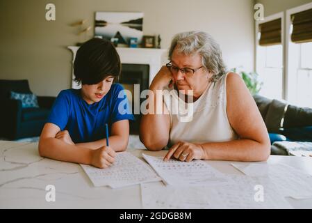 Grand-mère aidant petit-fils à écrire leurs devoirs à la maison. Banque D'Images