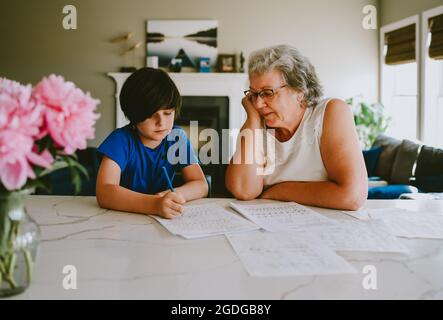 Grand-mère aidant petit-fils à écrire leurs devoirs à la maison. Banque D'Images