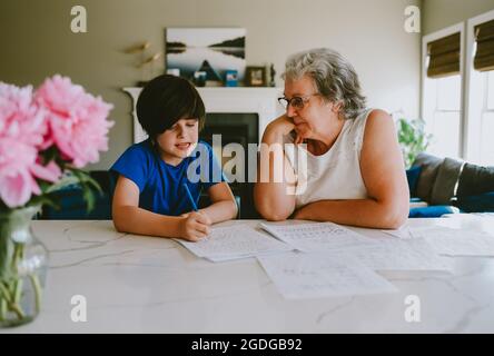 Grand-mère aidant petit-fils à écrire leurs devoirs à la maison. Banque D'Images