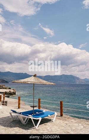 Des chaises longues se trouvent sous un parasol derrière une clôture donnant sur la mer Banque D'Images