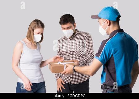 Livraison à domicile homme de messagerie portant l'uniforme et le masque de protection livrant le paquet au jeune couple en masques. Banque D'Images