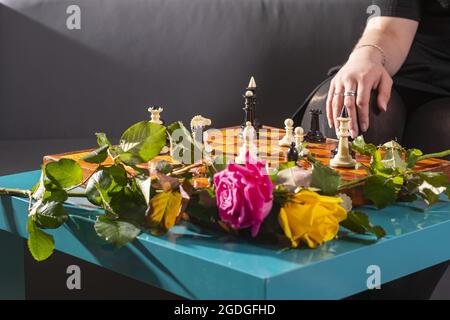 Échiquier avec figures placées, deux roses multicolores en gros plan. Main féminine en arrière-plan. Banque D'Images