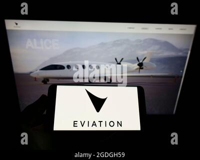 Personne tenant un téléphone portable avec le logo de la compagnie d'avions électriques Eviation Aircraft Ltd. À l'écran en face de la page Web. Mise au point sur l'affichage du téléphone. Banque D'Images