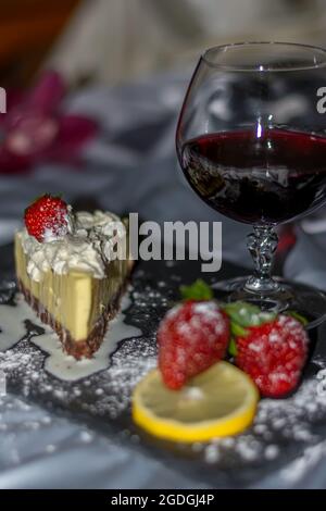 Morceau de gâteau au chocolat et à la crème délicate au citron et aux fraises. Un verre de vin rouge avec des fraises et des oranges partagé avec un être cher Banque D'Images