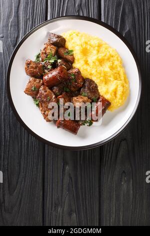 Le plat roumain pomana porcului se compose habituellement de diverses coupes de porc et d'abats, saucisses servies avec polenta gros plan dans une assiette sur la table. Verti Banque D'Images