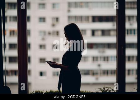 Femme d'affaires, jeune adulte, silhouette d'entraîneur debout à la fenêtre du bureau et parlant sur le téléphone mobile Banque D'Images