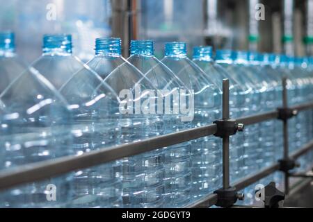 Vider les bouteilles en plastique bleues de cinq litres sur un tapis roulant. Production automatisée d'eau potable. Production alimentaire Banque D'Images