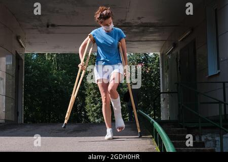 Une femme dont la jambe est cassée descend une rampe à l'aide de béquilles orthopédiques. Banque D'Images