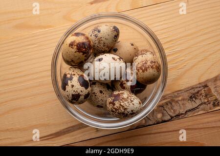 Plusieurs œufs de caille diététiques dans un bol en verre, gros plan, sur une table en bois, vue du dessus. Banque D'Images