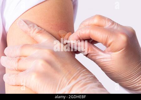 Médecin en gants médicaux de protection portant un bandage adhésif sur le bras de la femme après l'injection du vaccin en cas de pandémie. Banque D'Images