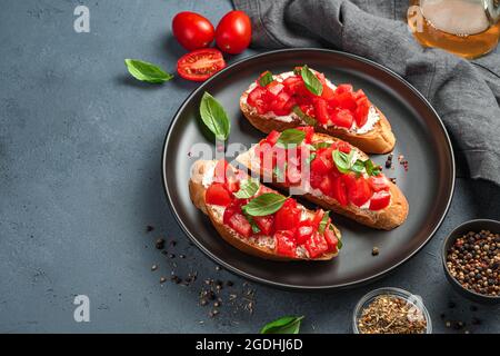 Trois bruschetta aux tomates, au basilic et au fromage sur une assiette noire. Banque D'Images