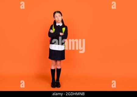 Pleine photo de corps de petite fille rêveuse regarder vide espace mains croisées sac isolé sur fond de couleur orange Banque D'Images