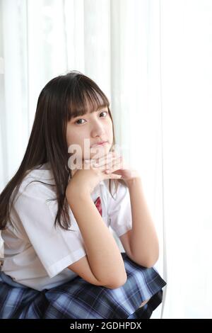 Portrait japonais école fille uniforme assis et regarder l'appareil photo dans une chambre aux tons blancs Banque D'Images