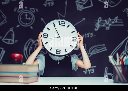 Une adolescente tient une grande horloge dans ses mains, la montre couvre son visage Banque D'Images