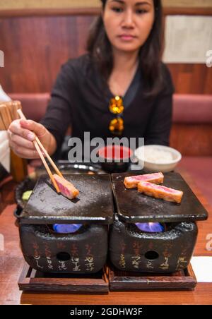 Femme cuisant du bœuf katsu sur un poêle traditionnel japonais en argile Banque D'Images