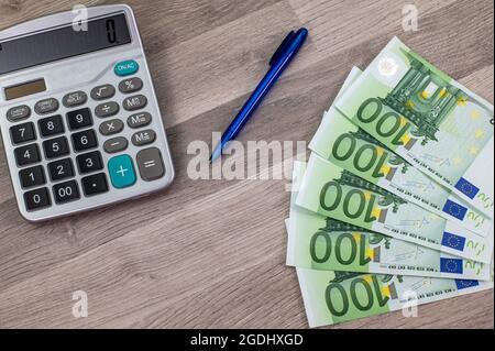 stylo calculatrice et 100 euros de factures sur une table en bois Banque D'Images