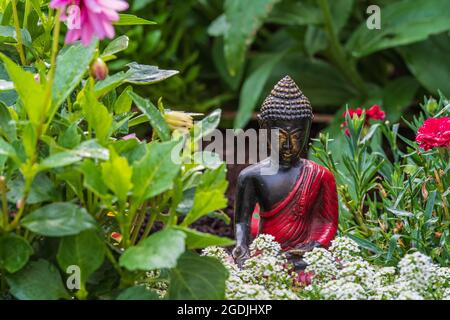 Photo de la figure de Bouddha noir dans un lit de fleurs entouré de différentes plantes. Banque D'Images